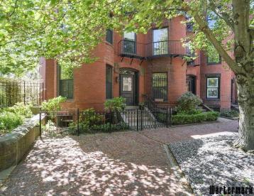 Red-brick brownstone with bay windows behind a wrought-iron railing